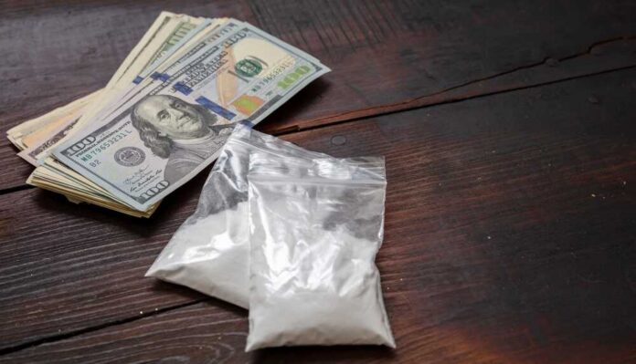 Bundles of cash next to bags of white powder on a wooden surface