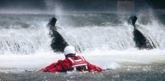 Rescuer in red gear navigating turbulent water near a waterfall