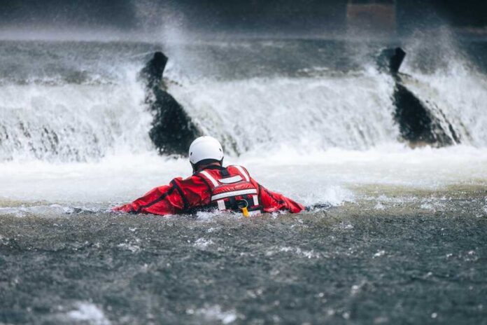 Rescuer in red gear navigating turbulent water near a waterfall