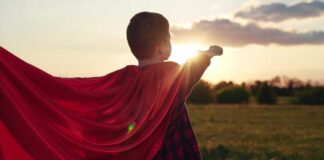 Child wearing a red cape standing in a field during sunset