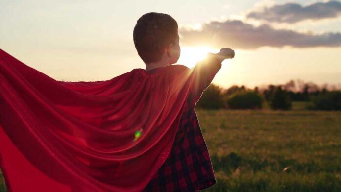 Child wearing a red cape standing in a field during sunset