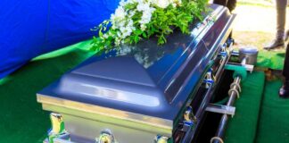 A silver casket adorned with flowers at a gravesite