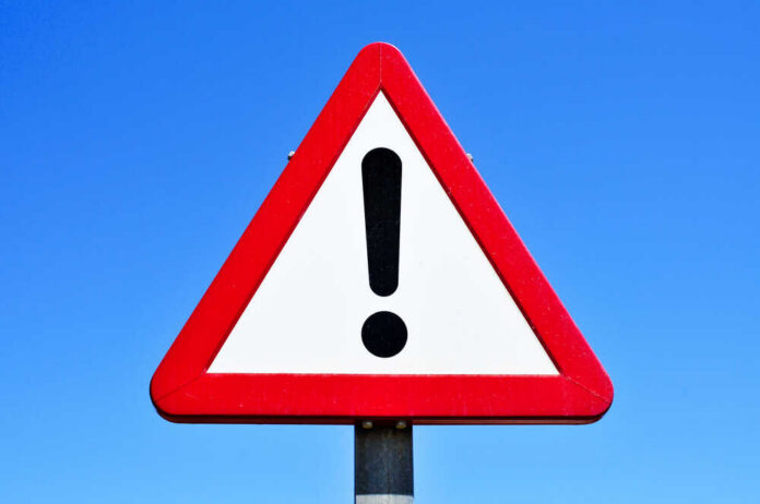 A triangular warning sign with an exclamation mark against a blue sky