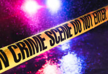 Crime scene tape with flashing lights in background.