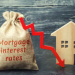 A burlap sack labeled Mortgage interest rates next to a wooden house and a downward red arrow