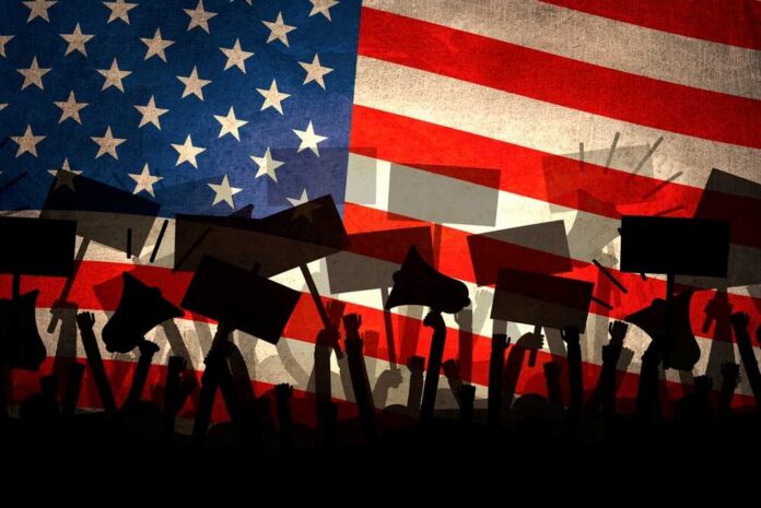 Silhouettes of protesters holding signs in front of an American flag