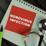Red card with 'NOROVIRUS INFECTION' text on a notebook with a stethoscope and pens