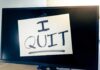 A computer monitor displaying a handwritten note that says 'I QUIT'