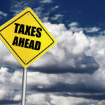 Yellow road sign reading taxes ahead clouds background