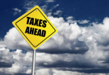 Yellow road sign reading taxes ahead clouds background