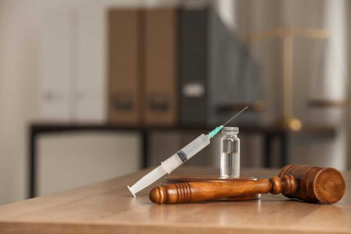 A syringe and vial placed next to a wooden gavel on a table
