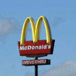 McDonalds drive-thru sign against a blue sky.