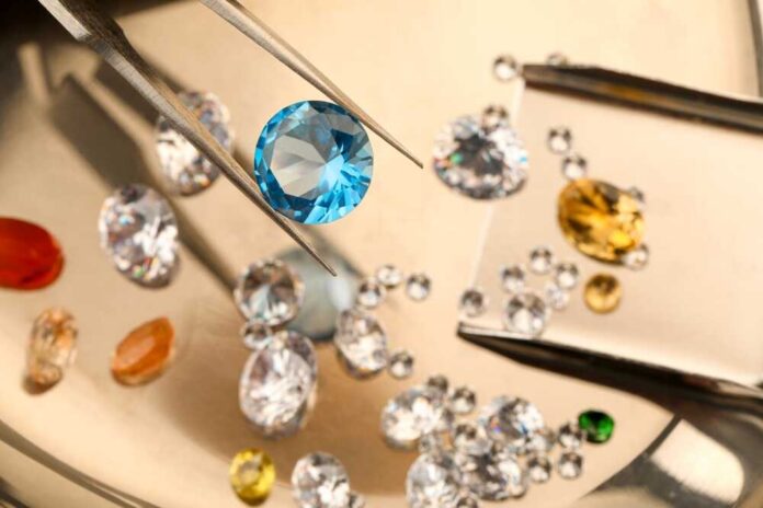 A blue gemstone being held with tweezers among various other gemstones