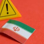Iranian Trigger Signal Sparks Sleeper-Cell Fears Iranian flag next to a caution sign on a red background
