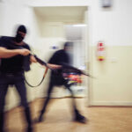 Armed Thugs Attack Packed Venue — Mass Panic Two masked individuals with guns moving quickly in a hallway