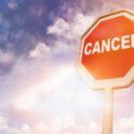 A stop sign with the word 'CANCER' against a cloudy sky