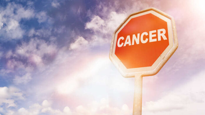 A stop sign with the word 'CANCER' against a cloudy sky