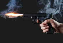 A hand holding a gun with smoke and a flash from the muzzle
