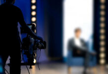 Person being filmed on a set with lights.