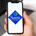 A hand holding a smartphone displaying the Sam's Club logo