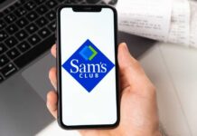 A hand holding a smartphone displaying the Sam's Club logo