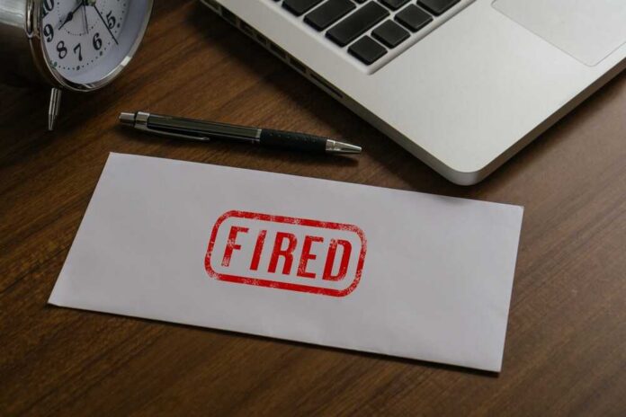 An envelope marked 'FIRED' on a wooden desk next to a clock and a laptop