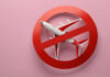 Airplane inside red prohibition sign on pink background.