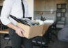 Person carrying box of office supplies in workspace.