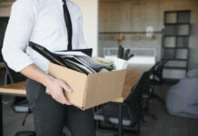 Person carrying box of office supplies in workspace.