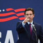 Governor of Florida, Ron DeSantis points forward at podium.
