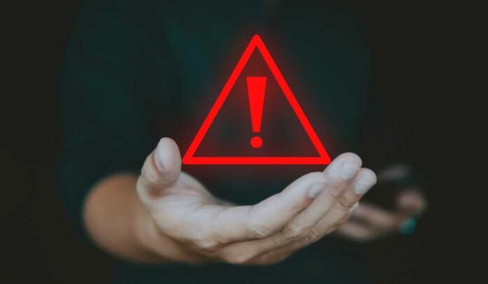 A hand holding a red warning triangle with an exclamation mark