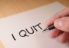 A hand writing 'I QUIT' on a piece of paper