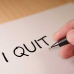 A hand writing 'I QUIT' on a piece of paper