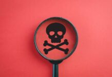 Magnifying glass focusing on a skull and crossbones symbol against a red background