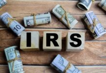 Wooden blocks spelling IRS surrounded by rolled currency notes