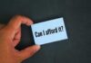 A hand holding a blue card with the text 'Can I afford it'
