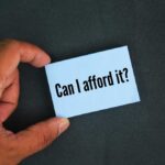A hand holding a blue card with the text 'Can I afford it'