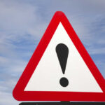 Warehouse Horror: Imported Animals Dead A triangular warning sign with an exclamation mark against a blue sky