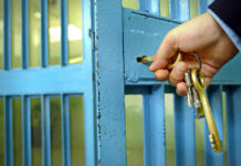 Hand unlocking blue metal door with keys.