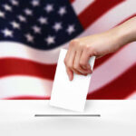 Hand dropping ballot into box, American flag background.