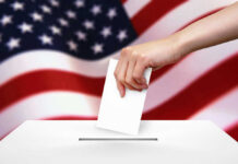 Hand dropping ballot into box, American flag background.