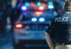 Violence Erupts: 5 Cops Struck By Vehicle Police officer stands near patrol car with lights flashing.