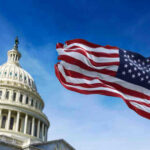 US Capitol with American flag waving in foreground.