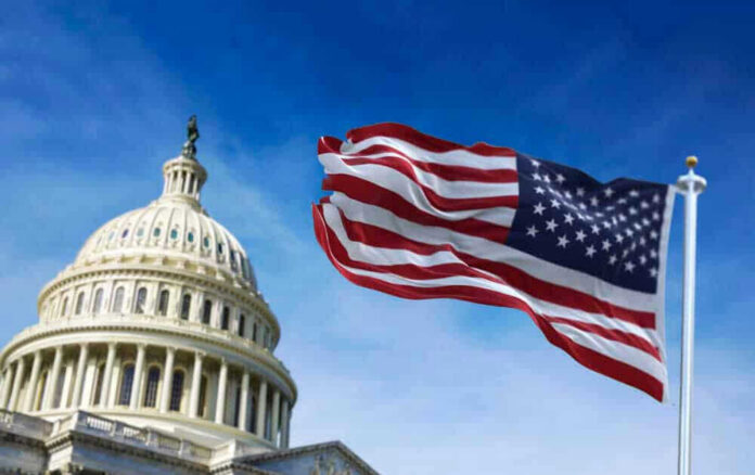 shutterstock_1915477927-1 US Capitol with American flag waving in foreground.