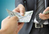 DOJ Drops Bombshell: Billionaire’s Case Wiped Clean A person handing over a stack of cash to another individual in a suit