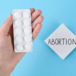 Supreme Court’s Role in Abortion Pill Chaos A hand holding a blister pack of white pills next to a note that says 'ABORTION'