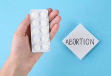 A hand holding a blister pack of white pills next to a note that says 'ABORTION'