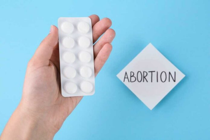 A hand holding a blister pack of white pills next to a note that says 'ABORTION'