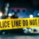 From All-American to DEAD at 29 Police line caution tape at a crime scene with blurred figures in the background