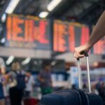 Inside CDC’s Urgent Ebola Volunteer Plea A traveler holding a suitcase in an airport terminal with a flight information display in the background